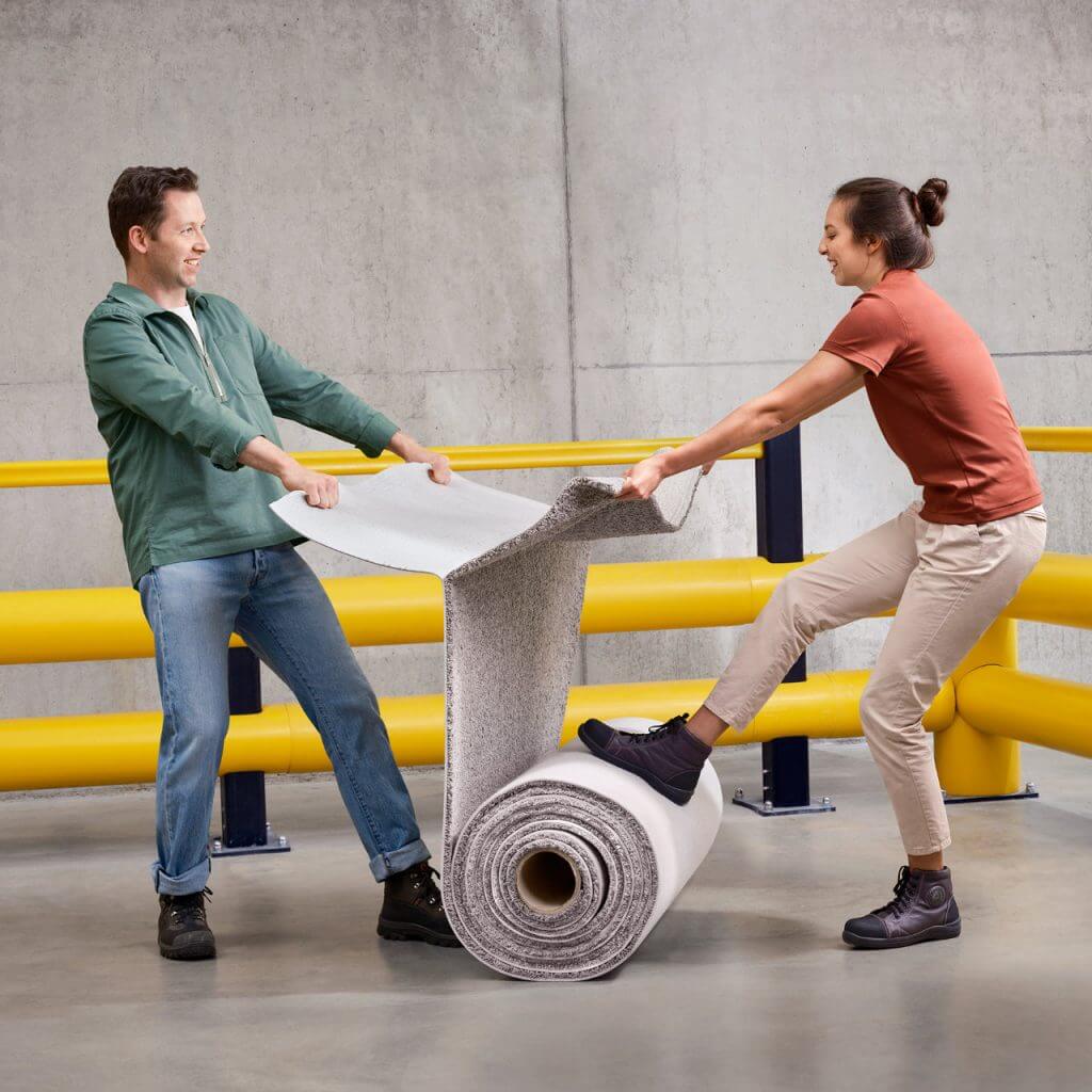 Two people standing pulling apart a roll of carpet, symbolizing Niaga click-unclick adhesive.